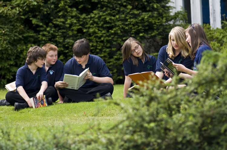 Students reading books on the grass in the grounds.